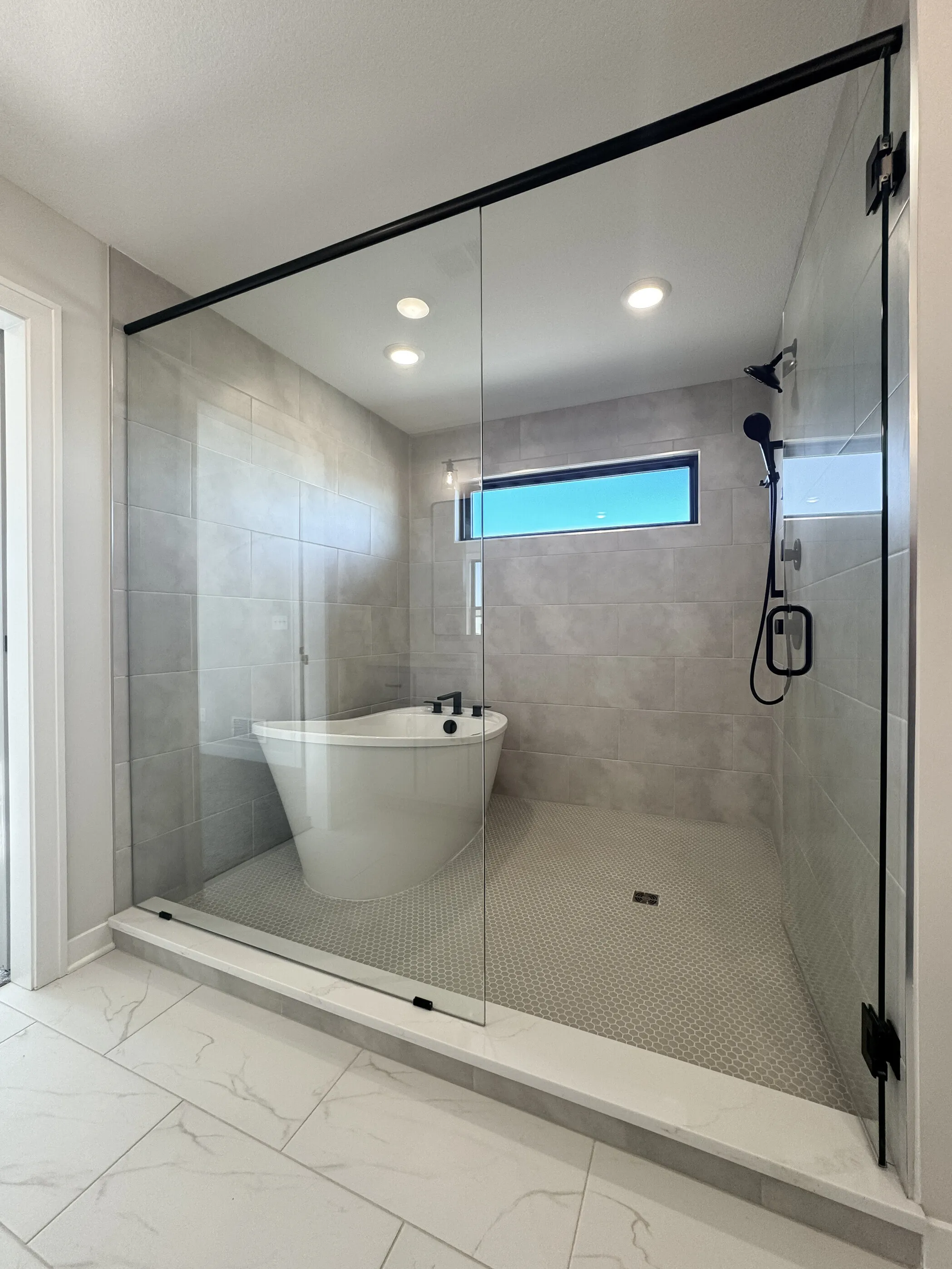 Wet-room with freestanding soaker tub and rain shower behind frameless glass enclosure