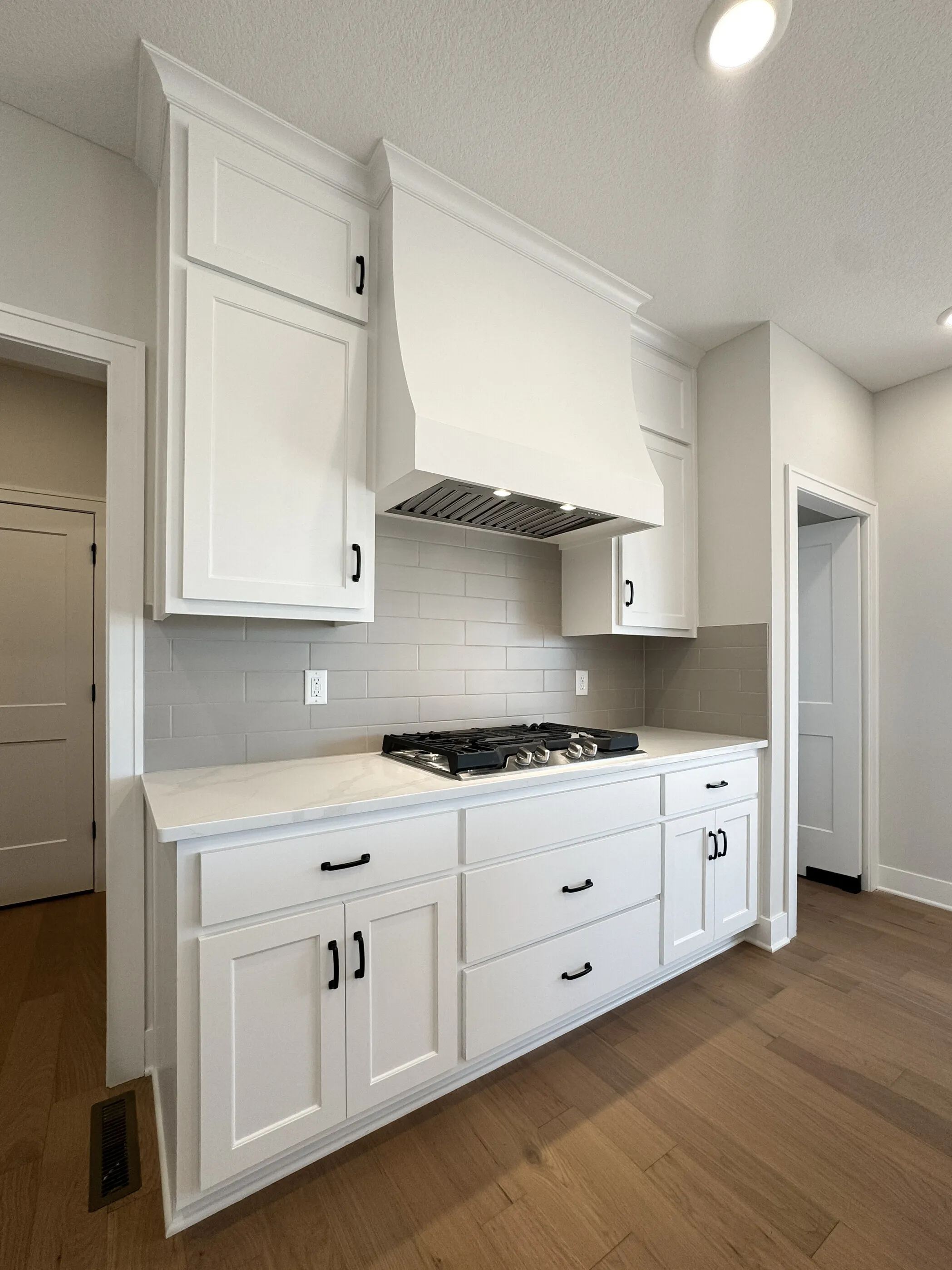 White shaker kitchen with custom range hood, gas cooktop, subway tile backsplash, and quartz counters